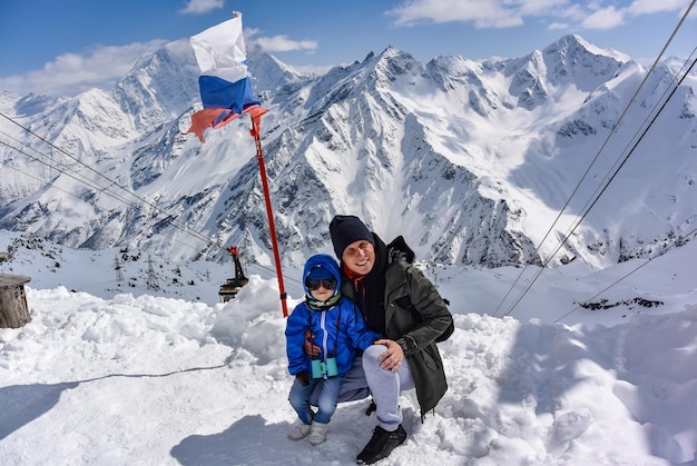 Un niño pequeño y un hombre en el fondo de montañas nevadas y la bandera de Rusia Elbrus 2019