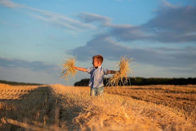 Un niño pequeño juega en un campo de trigo contra el fondo de un cielo azul y una luna