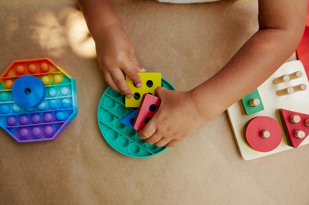 El niño pequeño juega con un colorido juguete sensorial antiestrés, empuje, pop it Juguete pop it de moda para el desarrollo de habilidades motoras finas Fidget sensorial Rainbow Nuevo juguete de silicona de moda y juguetes ecológicos de madera