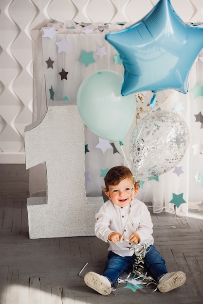 Niño pequeño juega con globos azules antes del gran número uno en una habitación acogedora