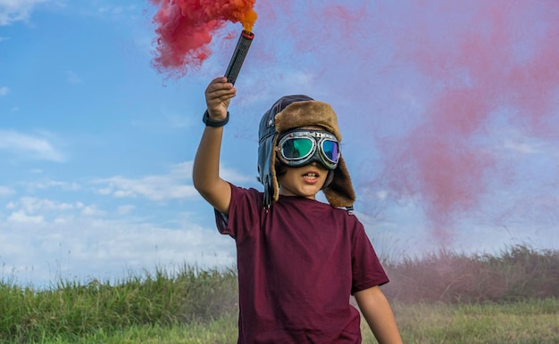 Niño pequeño juega con humo de colores, con un sombrero de aviador de los años 20 y gafas de piloto de avión