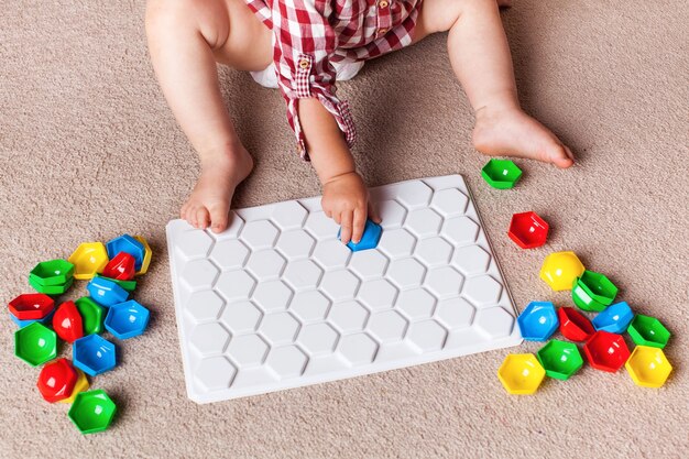 Un niño pequeño juega con un mosaico de plástico en la alfombra del cuarto de los niños. Desarrollo temprano, el método Montessori.