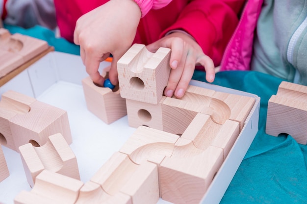 Un niño pequeño juega con un niño de preescolar constructor de madera aprendiendo en casa a hacer mosaico Desarrollo temprano Jugando y aprendiendo Las manos de los niños recogen el concepto de actividad de los cubos del constructor