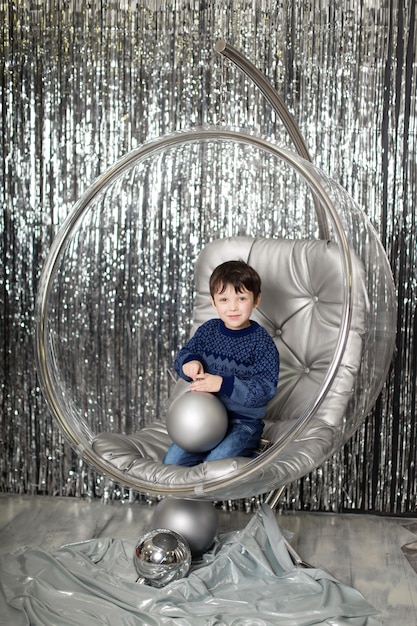 Niño pequeño juega en una silla un bol de cristal con bolas de plata