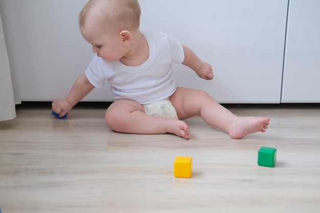 Un niño pequeño juega en el suelo con cubos de colores y construye una pirámide con ellos.