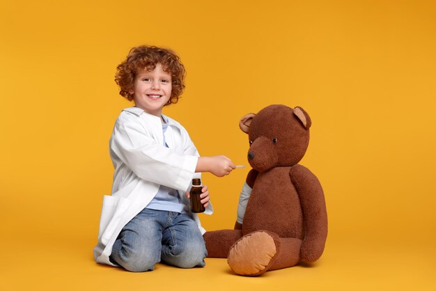 Niño pequeño jugando al doctor con un oso de juguete en fondo amarillo