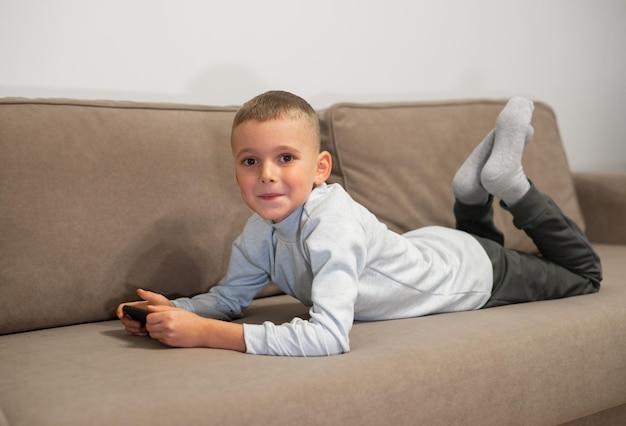 Niño pequeño jugando al juego móvil en el teléfono inteligente sentado en una vista superior del sofá Ocio infantil en video casero