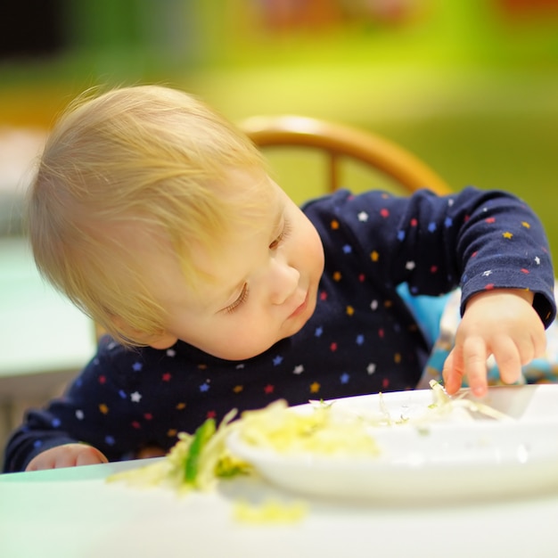 Niño pequeño jugando con comida en el café interior