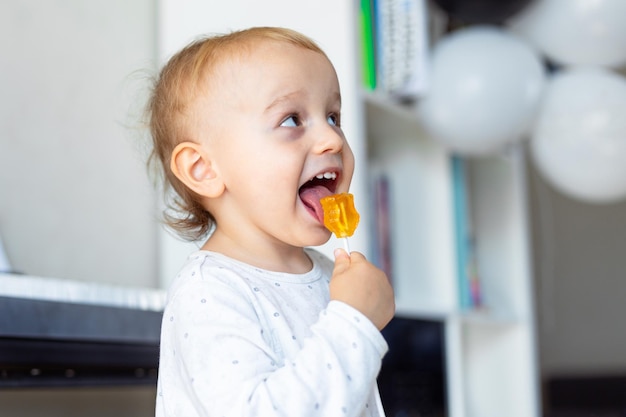 Niño pequeño lamiendo dulces piruletas azucaradas en casa cumpleaños mañana niño feliz