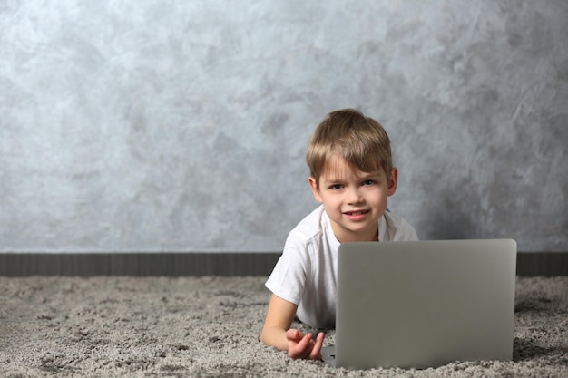 Niño pequeño con laptop en alfombra de piel contra fondo de pared gris
