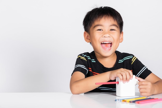 Un niño pequeño y lindo de 56 años sonríe usando sacapuntas mientras hace la tarea