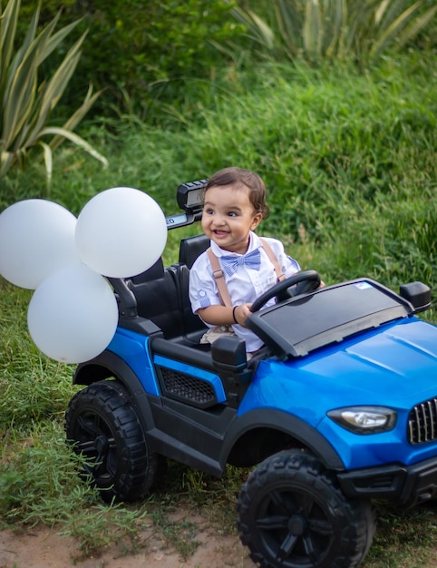 Foto niño pequeño lindo aislado con expresión facial inocente en un coche de juguete al aire libre desde un ángulo diferente