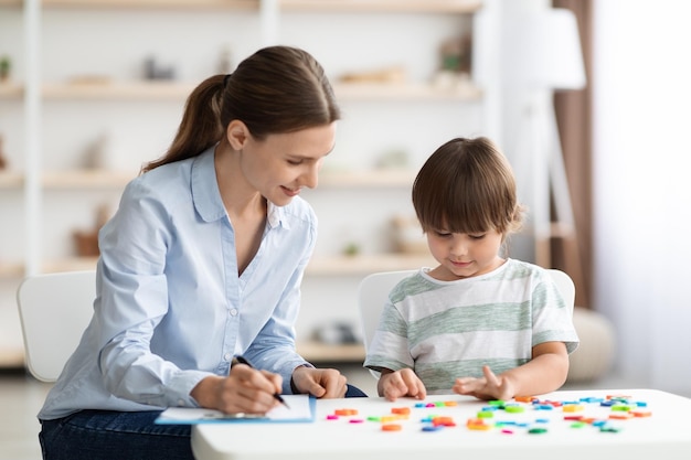 Un niño pequeño y lindo estudia para leer con un tutor profesional, una mujer positiva, un tutor que ayuda a los niños y toma