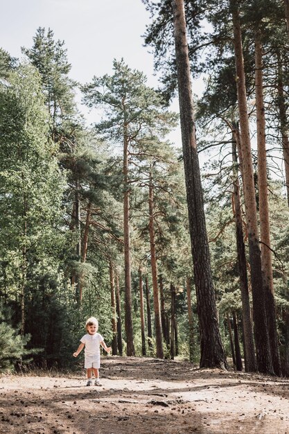 Niño pequeño lindo feliz en camiseta y pantalones cortos caminando por el camino en el parque de verano Niño pequeño de excursión en el camino en el bosque de pinos Concepto de viaje hiperlocal Estilo de vida activo Niño divirtiéndose en bosques verdes