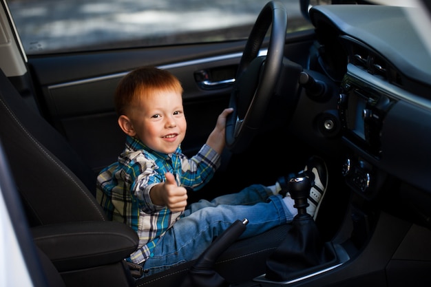 Niño pequeño lindo que conduce el coche de los padres