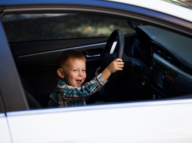 Niño pequeño lindo que conduce el coche de los padres