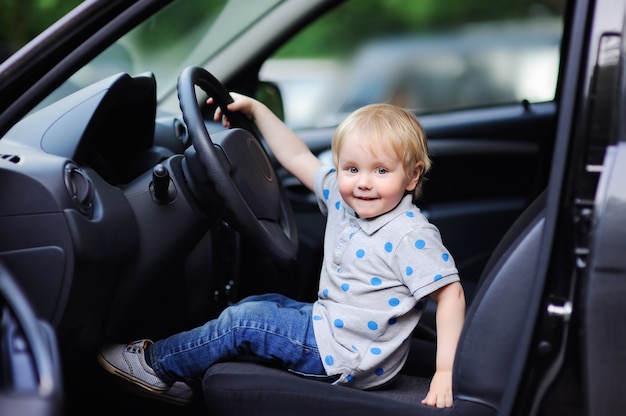 Niño pequeño lindo que juega en el coche de los padres