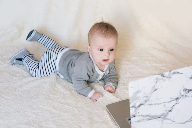 Niño pequeño lindo que miente y que mira en la computadora portátil