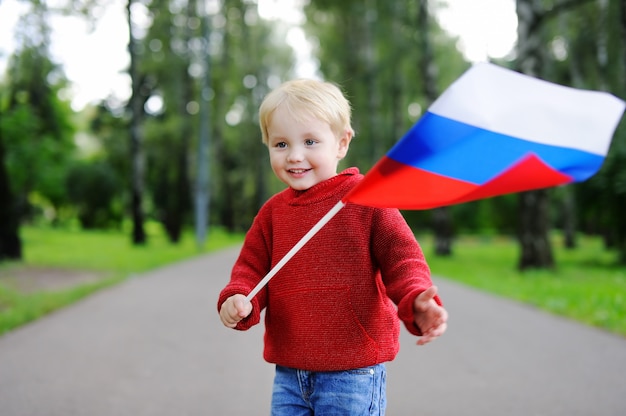 Niño pequeño lindo que sostiene la bandera rusa al aire libre