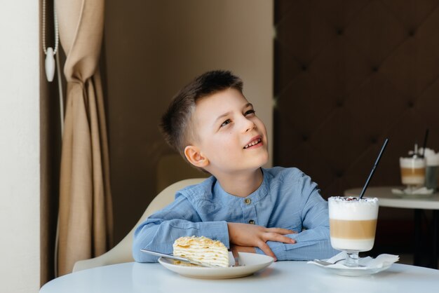 Foto un niño pequeño lindo está sentado en un café y mirando un pastel y primer plano de cacao. dieta y nutrición adecuada.