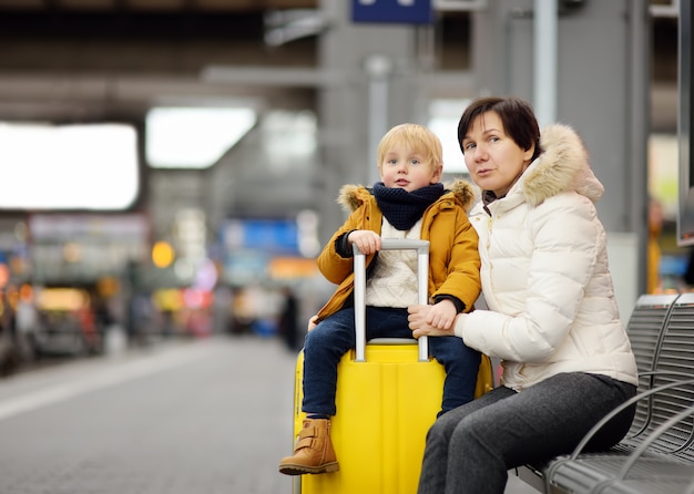 Niño pequeño lindo y su tren expreso que espera de la abuela / de la madre en la plataforma de la estación de ferrocarril