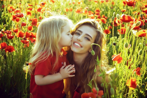 Niño pequeño a la madre o hermana besada en campo de amapolas.