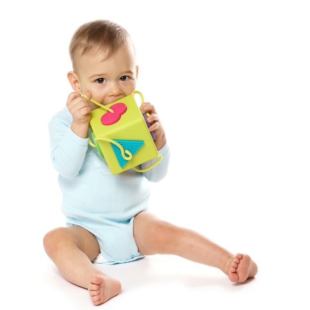 Niño pequeño en mameluco sentado y jugando con juguete de plástico