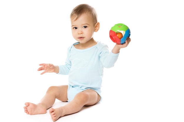 Niño pequeño en mameluco sentado y jugando con juguete de plástico