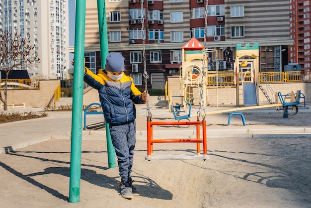 Un niño pequeño con una máscara camina en el patio de juegos durante la cuarentena. Quédate en casa