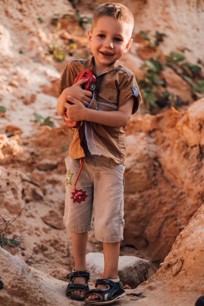 Un niño pequeño se para en medio de la arena y sostiene un juguete en sus manos.