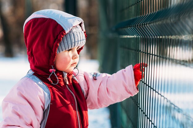 Niño pequeño mira a través de los barrotes en invierno