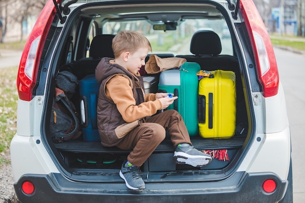 Niño pequeño mirando una bolsa de papel con dulces sentados en el baúl del auto lleno de bolsas.