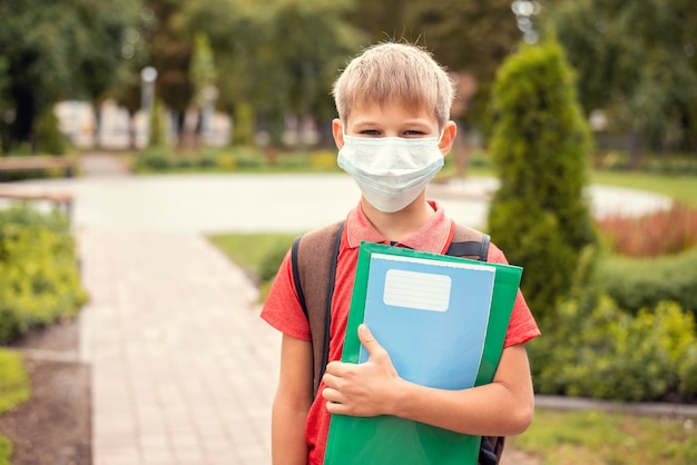 Niño pequeño con mochila y máscara protectora en el parque de camino a la escuela