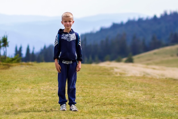 Niño pequeño con una mochila de senderismo en verano escénico verde montañas de los Cárpatos. Niño de pie solo disfrutando de vistas al paisaje de montaña. Concepto de estilo de vida activo, aventura y actividad de fin de semana.