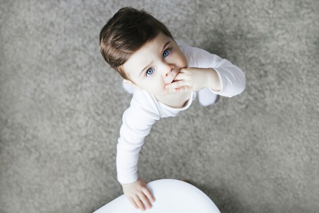 Niño pequeño en mono blanco de pie sobre una alfombra