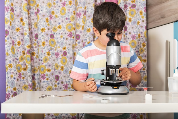 Niño pequeño muchacho caucásico mirando a través del microscopio en la escuela