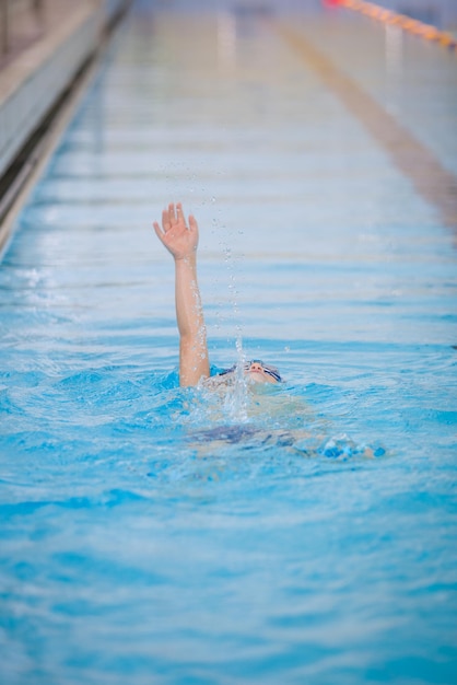 Un niño pequeño nada en una piscina al estilo de un golpe de espalda con todo el cuerpo en el agua en el interior