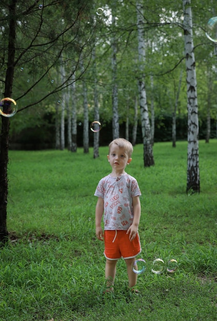 niño pequeño en la naturaleza mira pompas de jabón