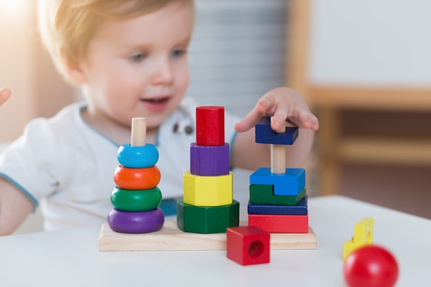 Niño pequeño niño jugando pirámide de juguete de madera en casa o jardín de infantes