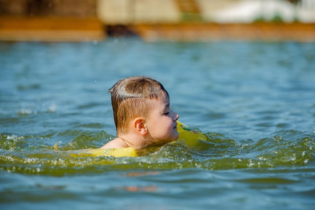 Niño pequeño niño nadando en el lago con apoyo de ayudas de brazos inflables