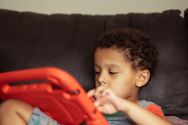 Niño pequeño o preescolar diverso en casa en el sofá usando una tableta