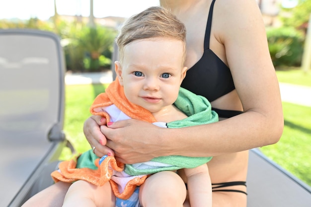 Foto niño pequeño con ojos azules envuelto en una toalla después de nadar en la piscina.