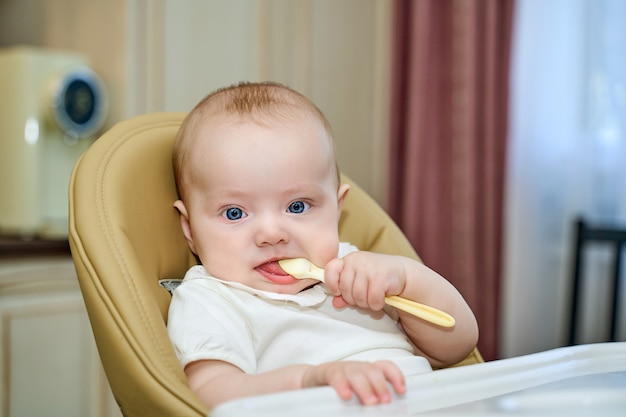 Un niño pequeño con ojos azules sostiene una cuchara sentado en una silla alta