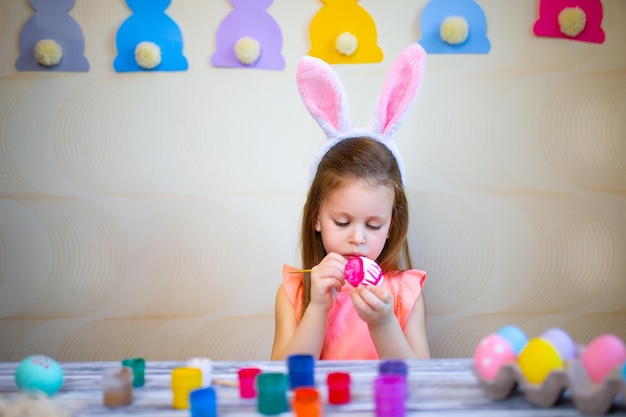 Niño pequeño con orejas de conejo de pascua pintando huevos de pascua en casa se prepara para pascua felices pascuas