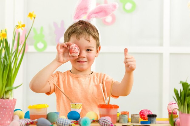 Niño pequeño con orejas de conejo de Pascua pintando huevos de Pascua