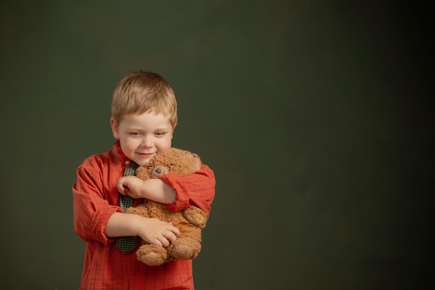 Foto niño pequeño con oso de peluche y maleta vieja sobre fondo oscuro