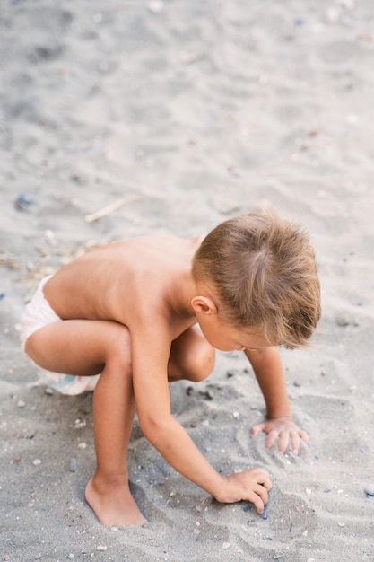 Un niño pequeño con pañales está jugando en la playa de arena durante las vacaciones de verano