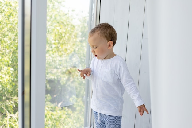 Un niño pequeño parado en la ventana y esperando a mamá y papá.