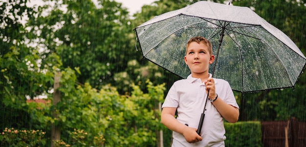 Niño pequeño con paraguas y de pie bajo la lluvia