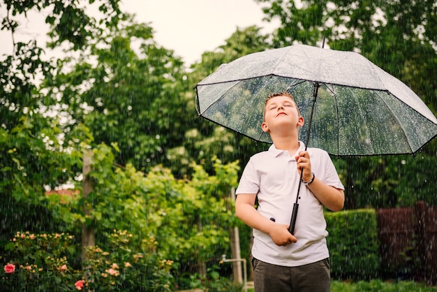 Niño pequeño con paraguas y de pie bajo la lluvia